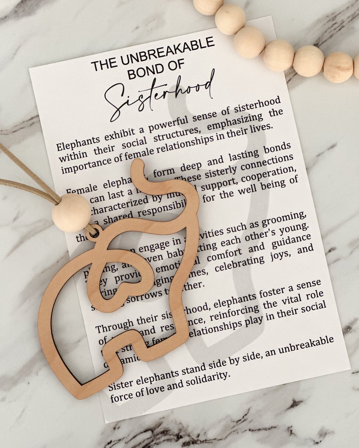 Wooden elephant charm on a marble surface with text about sisterhood.