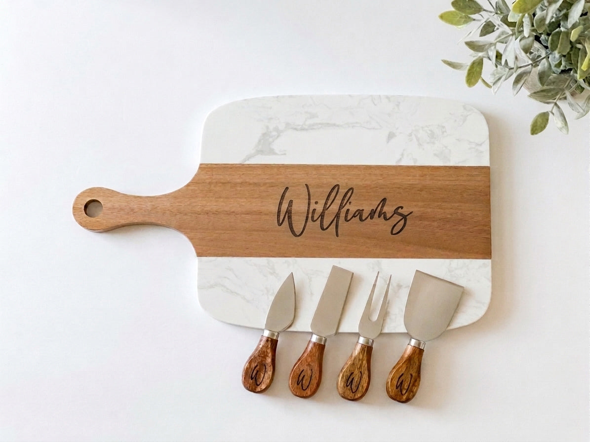 Marble and wood cutting board with engraved name and four cheese knives on a white background